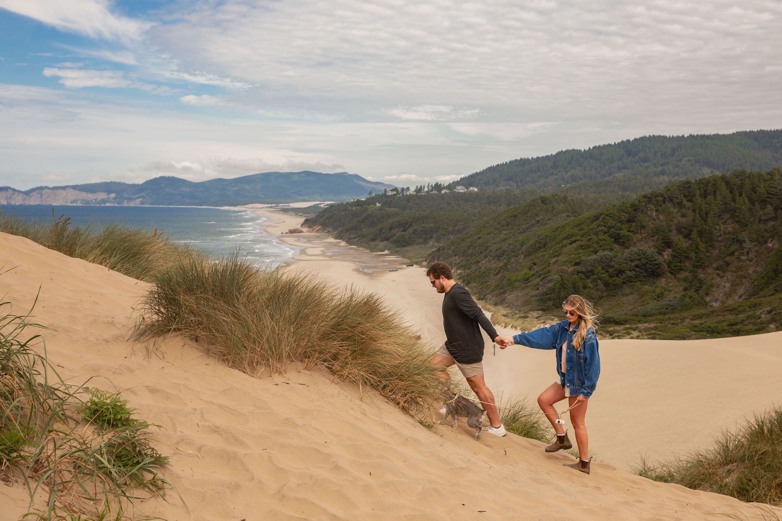 A couple walking up a dune holding hands near Inn at Cape Kiwanda