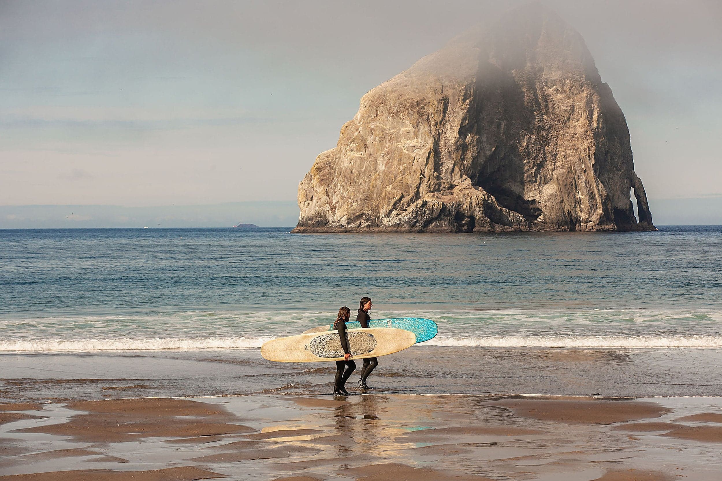 Surfers on the beach at Cape Kiwanda with Haystack Rock in the background, Pacific City, Oregon — Inn at Cape Kiwanda.
