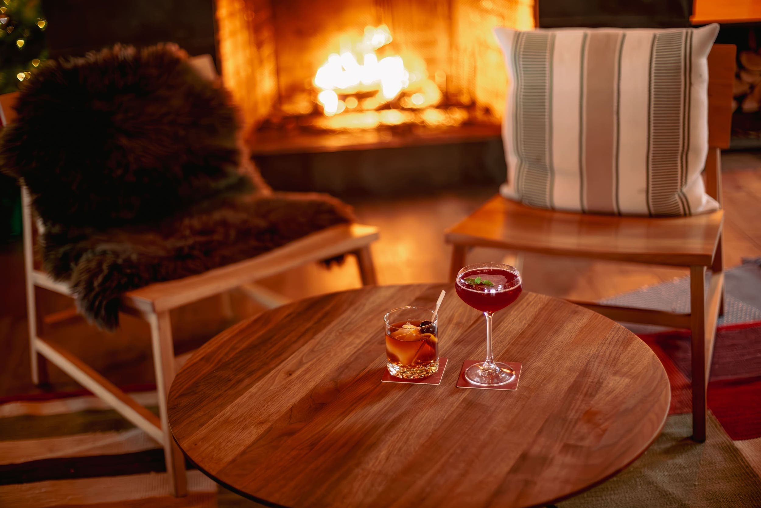 A small wooden table close to a fireplace with two cocktails on it at Headlands