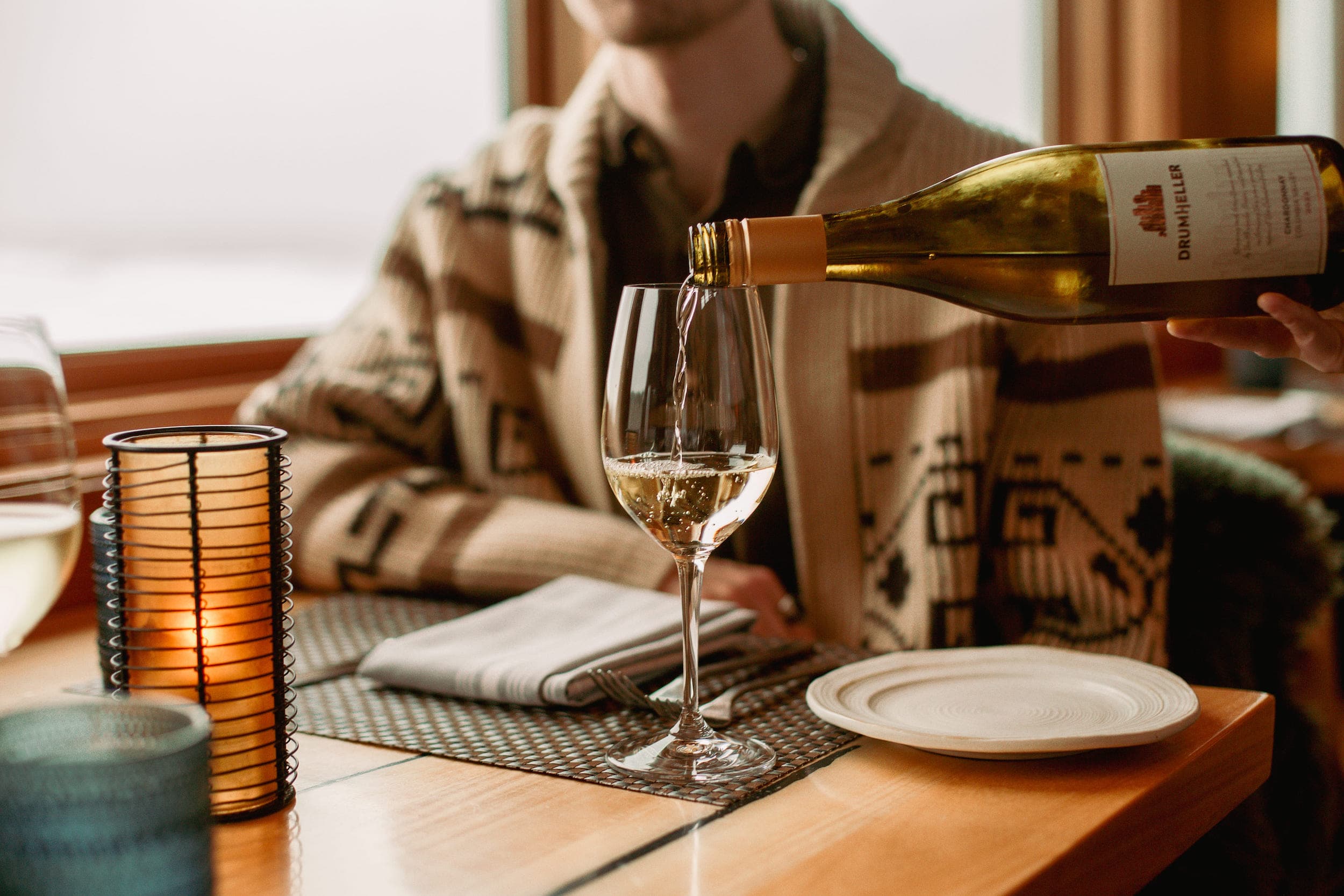 A server pouring a glass of white wine for a man sitting at a table