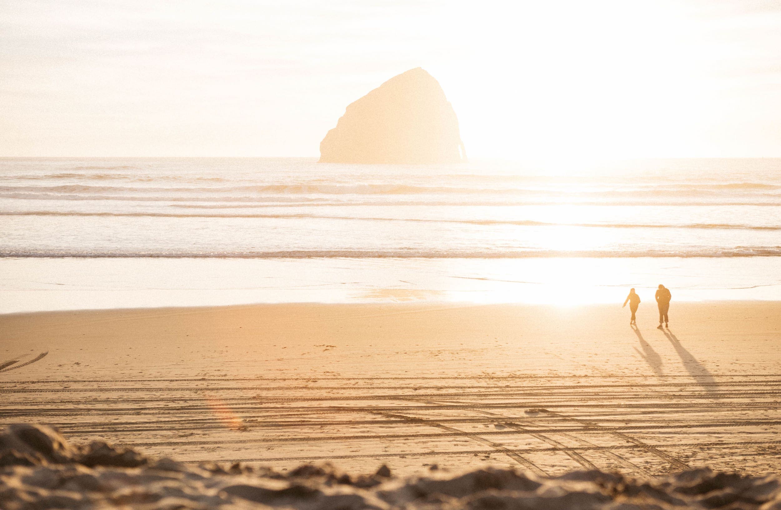 Two people walking on the beach with the sun bleaching out the beach and water